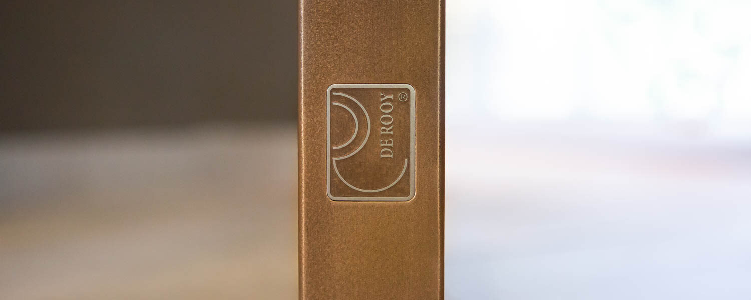 Logo van De Rooy op een bronzen stalen deur, symbool van vakmanschap.